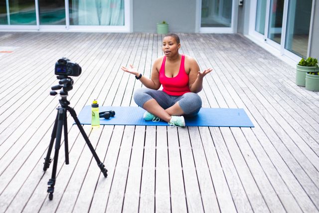 African american female blogger recording a video on digital camera while sitting on yoga mat. fitness and healthy lifestyle concept