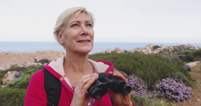 Senior woman spending time in nature, standing admiring the view using binoculars in slow motion. healthy lifestyle fitness retirement.