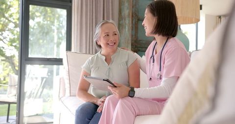 Nurse Consults Senior Woman While Smiling at Home with Clipboard