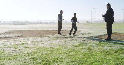 Senior Coach Guiding Diverse Male Players on Dewy Baseball Infield at Dawn Practice