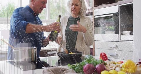 Senior couple cooking together at modern kitchen island pouring olive oil with vegetables