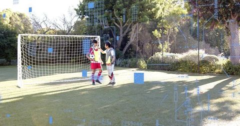 Youth coach instructing teenager holding ball by goal during outdoor soccer training