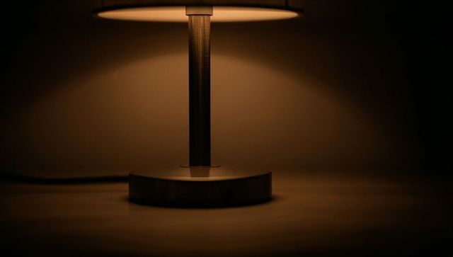 Modern table lamp casting warm amber glow on bedroom wall with visible power cord