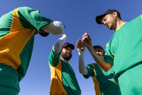 Baseball team raising hands in pre-game huddle wearing green yellow uniforms