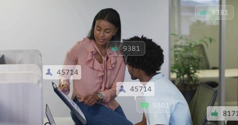 Two colleagues collaborating over tablet with social media metrics overlays in modern office