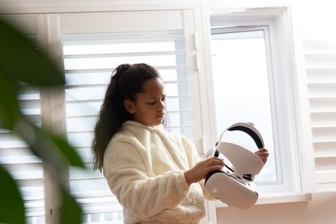 African american girl inspecting vr headset in cozy sunlit home near window shutters
