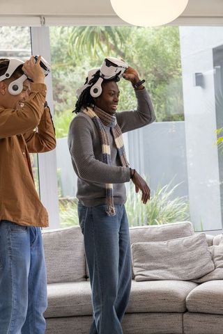 Friends removing and adjusting white vr headsets in bright living room for at-home gaming