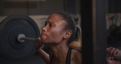 Athletic woman performing intense barbell squat in gym