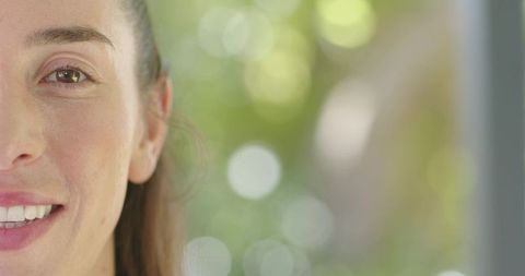 Smiling woman looking through window with green bokeh background, half-face portrait