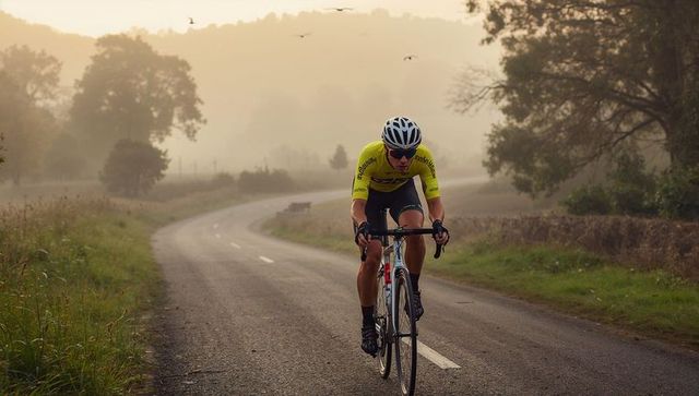Cyclist riding through misty country road wearing yellow jersey and white helmet