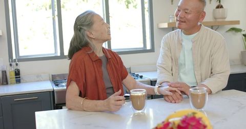 Mature couple sharing morning coffee while holding hands at sunlit kitchen island