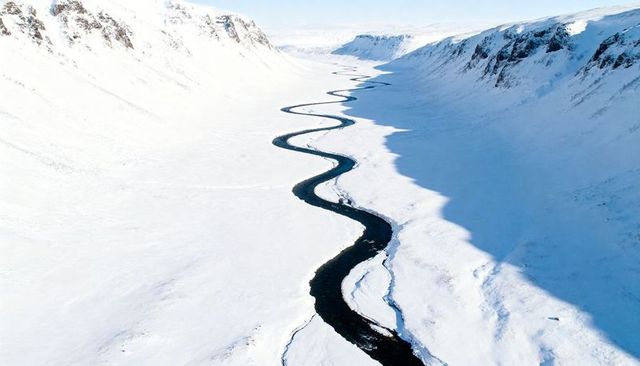Sinuous black river winding through snow-filled alpine valley with serpentine meanders