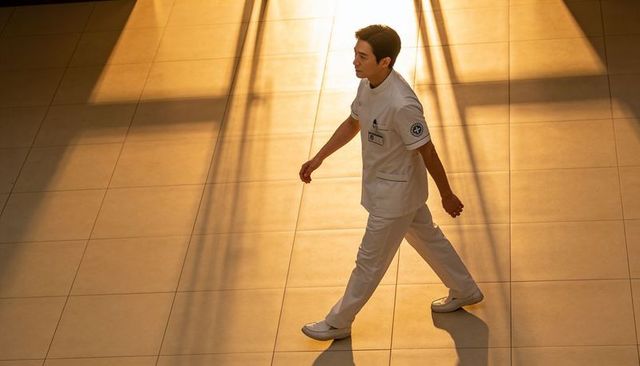 Male healthcare worker walking in sunlit hospital lobby casting dramatic shadows