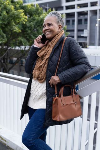 Senior african american woman talking on phone while leaning on urban bridge railing