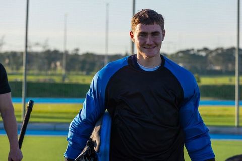 Youth Field Hockey Goalkeeper Stands Confidently on Pitch