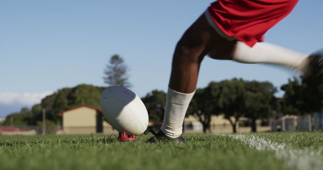 Image shows athlete's leg in motion while kicking rugby ball on grass field. Suitable for sports articles, rugby training guides, sports equipment ads, and athletic event promotions.
