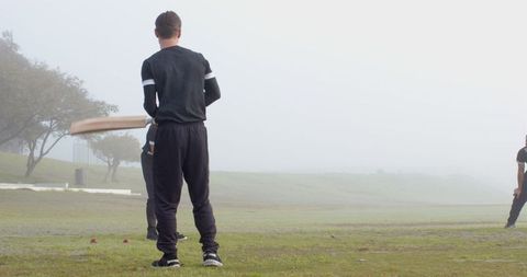 Cricket practice in misty field with teammates in black