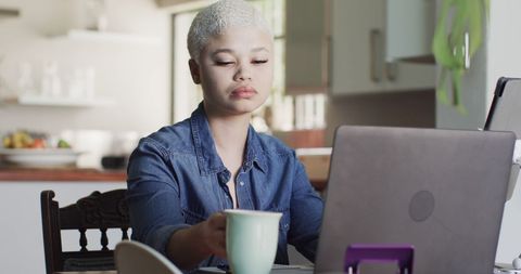 Biracial woman using laptop while drinking coffee at home