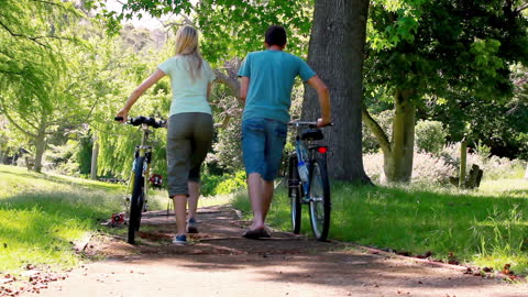 Couple Walking Bicycles in Sunlit Park