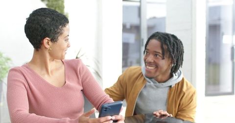 Smiling diverse coworkers collaborating at modern bright office table with smartphone