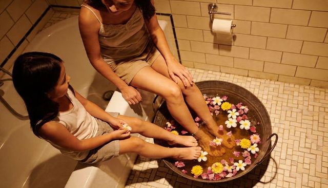 Mother and daughter soaking feet in flower-filled footbath for cozy evening bonding