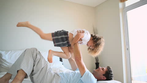 Father and Son Laughing and Playing on Bed at Home
