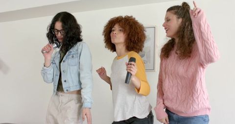 Diverse friends singing karaoke in cozy living room, casual trio having fun