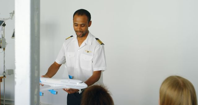 Pilot in uniform presenting an aircraft model to a group of students in a classroom setting provides a clear depiction of aviation education and training. Useful for articles or marketing materials related to pilot schools, aviation education, or aviation workshops.