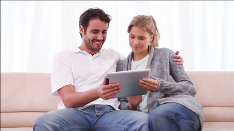 Happy Couple Sharing Tablet at Home Relaxing on Couch