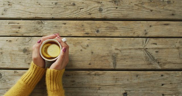 Image of hands of caucasian woman holding mug with tea and lemon on wooden surface. seasons, autumn, coziness and relax concept.