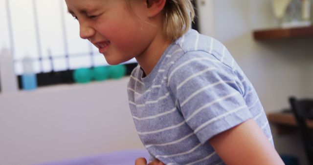 Young boy holding his stomach while appearing to be in pain indoors. Suitable for articles and content related to child health, stomach ache remedies, pediatric illnesses, distress and discomfort in children, or educational materials on recognizing symptoms of illness in children.