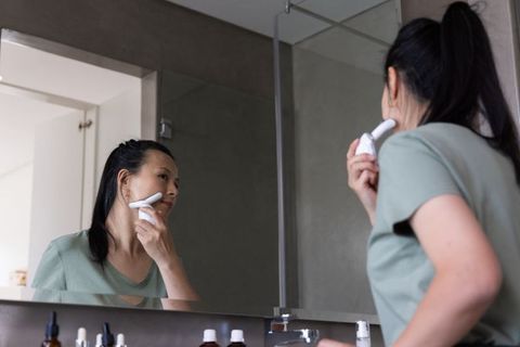 Middle-aged asian woman using handheld facial device at bathroom vanity during morning skincare rout