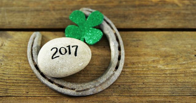 Stock photo depicting a lucky themed display with a clover, horseshoe, and a stone inscribed with the year 2017 on a wooden background. Perfect for use in New Year celebration materials, good luck charms advertisements, or themed website headers.