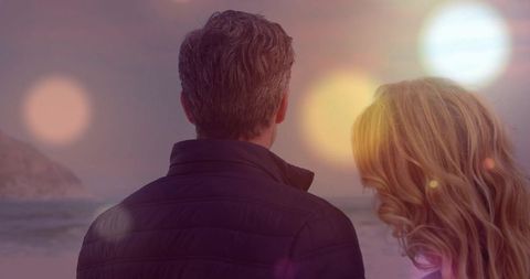 Couple watching sunset over ocean shoreline, romantic silhouette with lens flare