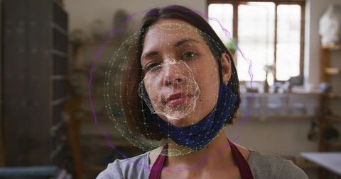 Potter inspecting 3d facial mesh overlay while wearing blue mask in light-filled workshop