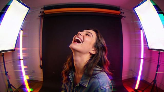 Joyful woman laughing, tilting head back in neon-lit studio portrait wearing denim jacket