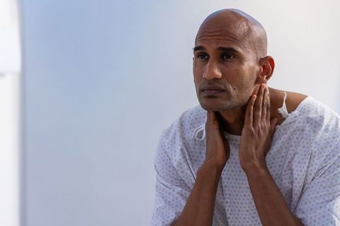 Contemplating african man wearing hospital gown touching neck, somber medical portrait
