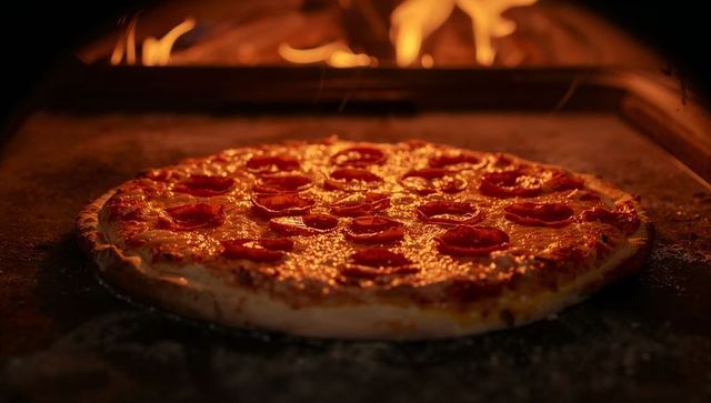 Wood-fired pepperoni pizza baking on stone oven with melting cheese and curling pepperoni