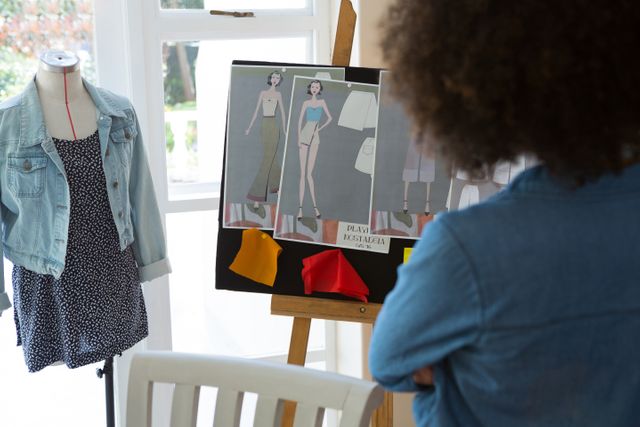 Fashion designer reviewing sketches and fabric samples on a bulletin board in a home studio. Ideal for use in articles or advertisements related to fashion design, creativity, home-based businesses, and the fashion industry.