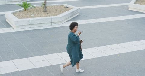 Positive Biracial Woman with Smartphone Walking on Urban Street