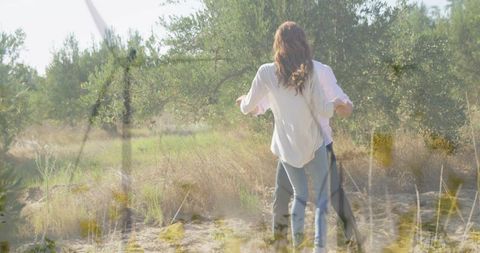 Couple embracing in sunlit olive grove walking through dry meadow, back view