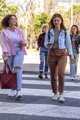 Diverse women walking across urban crosswalk laughing and checking smartphone