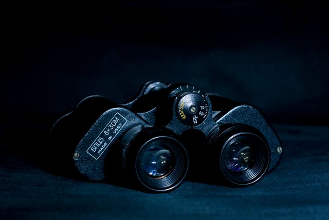 Vintage binoculars in dramatic lighting on dark background showcase classic design. Suitable for illustrating topics on exploration, adventure gear, wildlife observation, or vintage optical instruments.