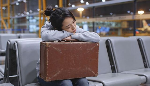 Tired solo traveler resting on vintage leather suitcase at quiet airport gate late night