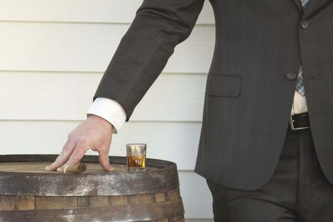 Businessman enjoying whiskey and cigar on rustic barrel