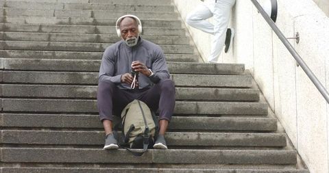 Senior african american man sitting on steps resting with backpack and wearing headphones