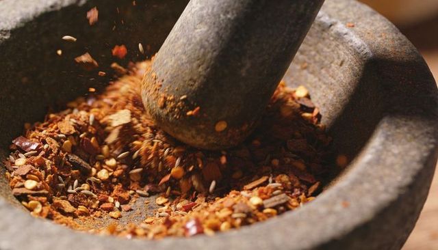 Granite mortar and pestle crushing mixed spices closeup — red pepper flakes and seeds