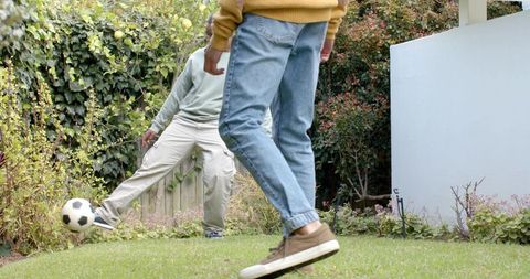 Diverse friends playing backyard soccer on lawn kicking ball casual outdoor game