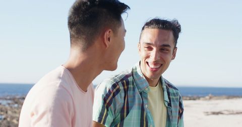 young men enjoying pleasant conversation outdoors by ocean, highlighting friendship and romantic bond during summer vacations. ideal for use in travel, relationship, and leisure contexts, this image captures warmth, happiness, and companionship in natural setting.