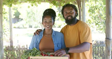 African couple harvesting fresh vegetables under sunlit pergola